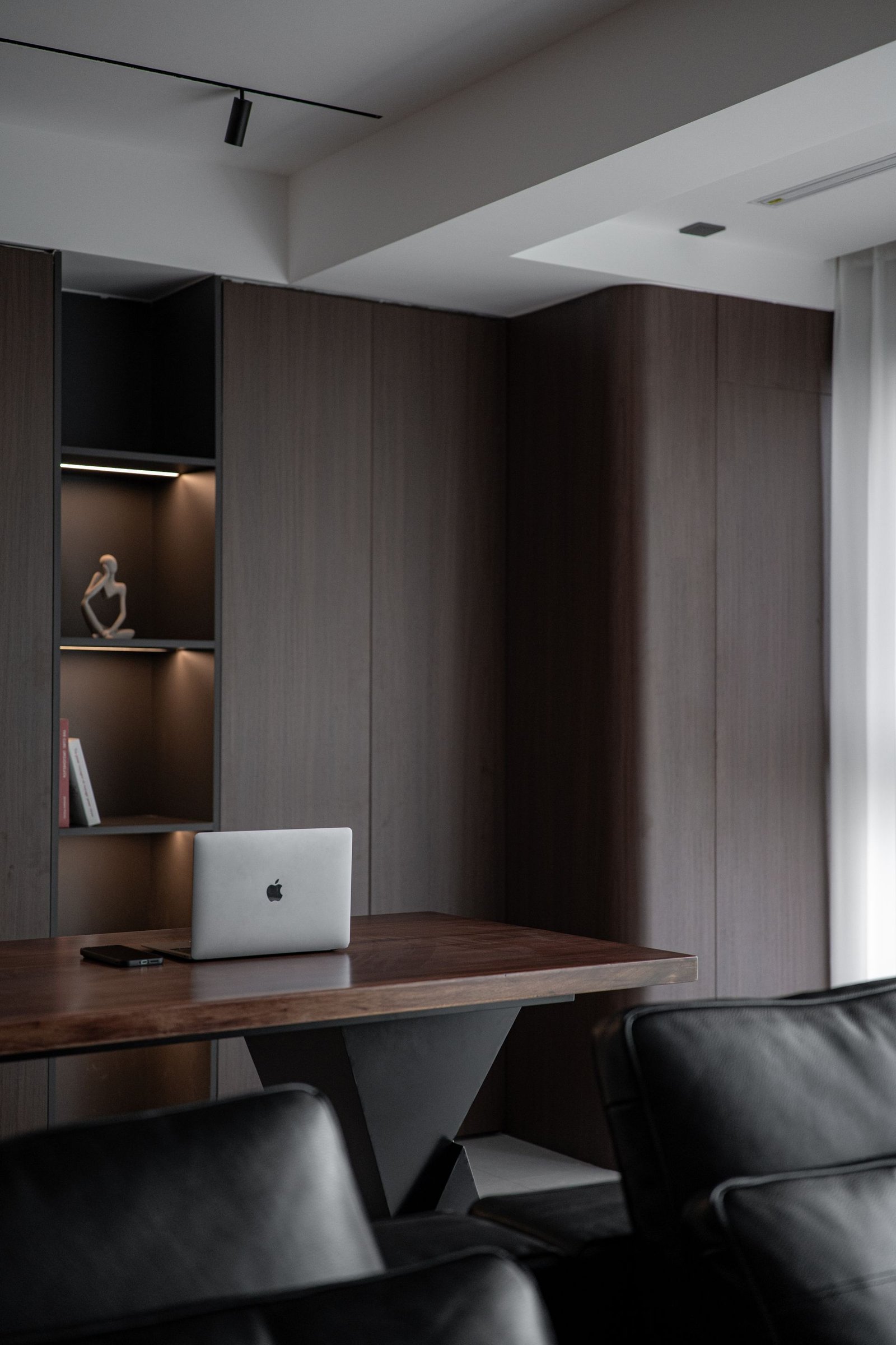 Executive office with a walnut desk, dark wood panelling and black leather seating